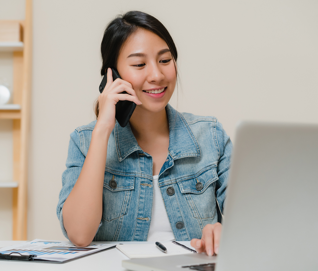 Asian business woman multitasking on a laptop and phone in a creative office
